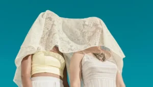Dos jóvenes cuyo rostro está oculto bajo una tela que cae como un mantel, creando un efecto visual intrigante