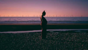 Mujer embarazada de pie en la playa al atardecer, contemplando su vientre