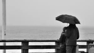 Dos personas de pie en un muelle, contemplando el mar en silencio